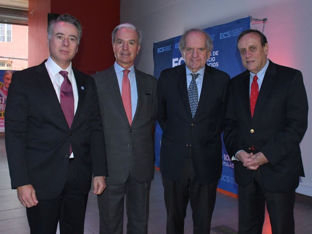 Four men in business suits posing for a photo at a formal event, with a blue banner in the background.