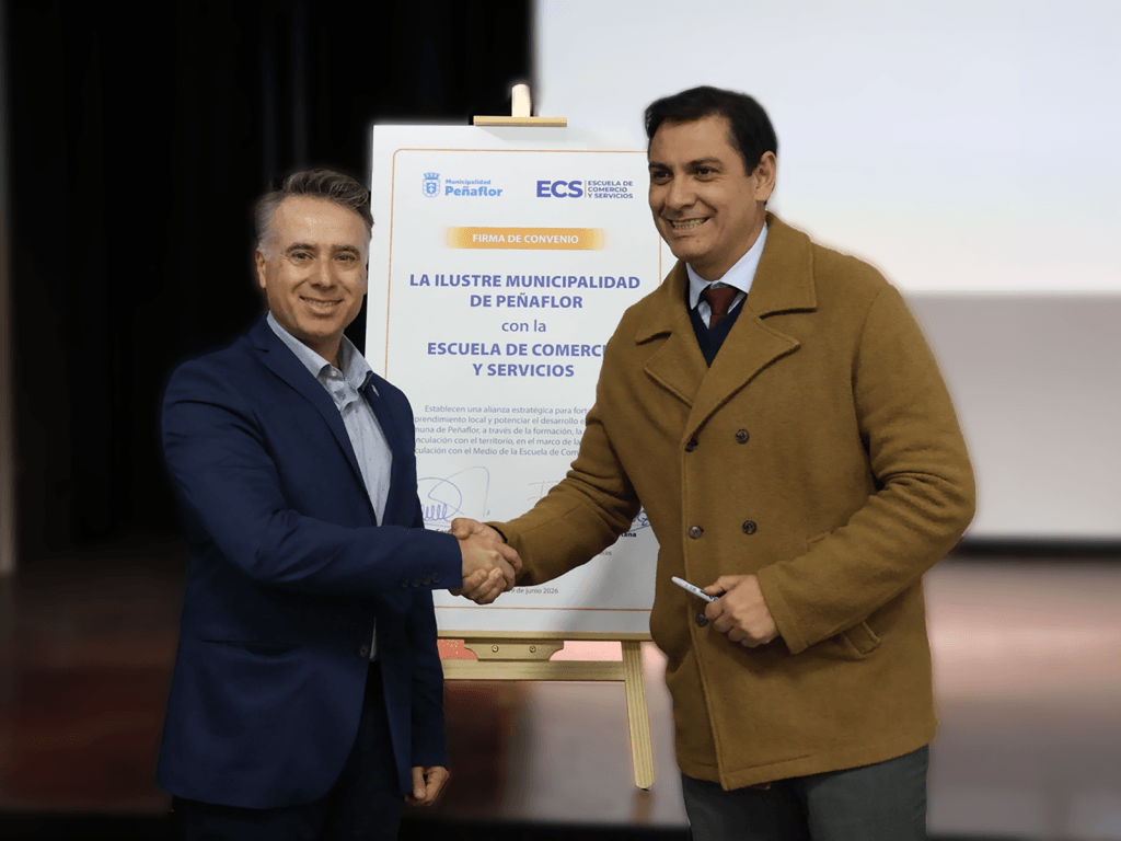 Two men in business attire shake hands in front of a poster announcing a municipal agreement in Peñaflor.